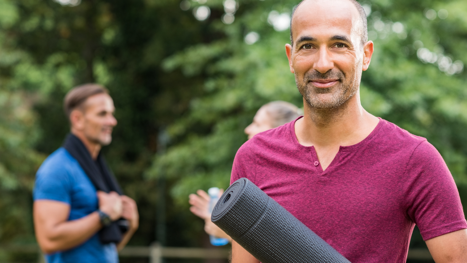 Smiling mature man holding yoga mat and looking at camera