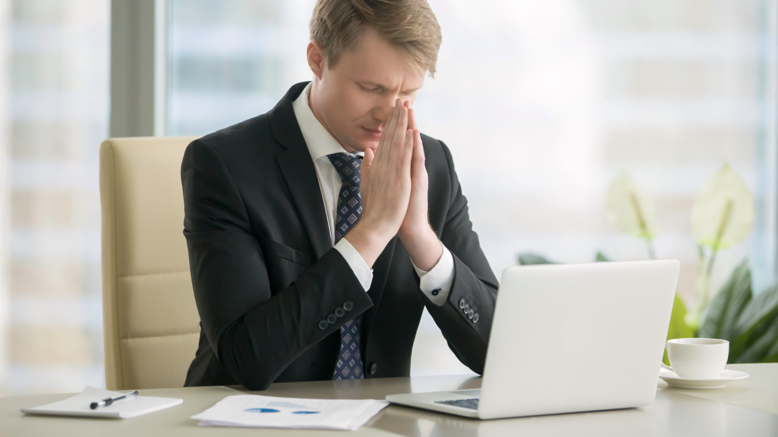 Young businessman working with laptop at desk, meditating, improving work - life balance, finding ways to increase productivity