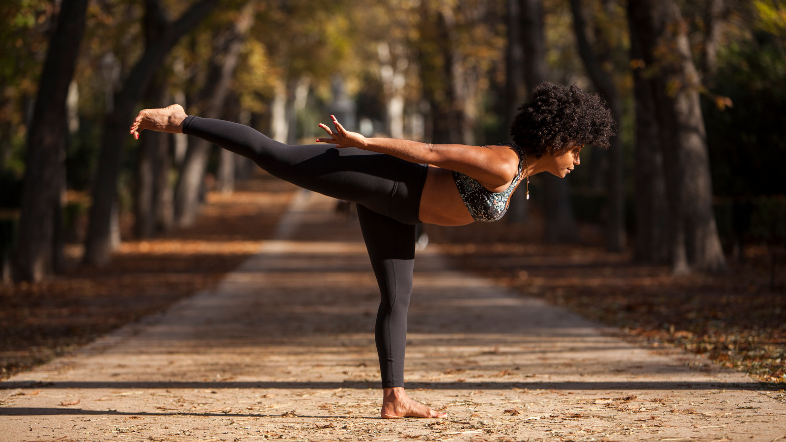 Beautiful African American woman practicing yoga outdoors, on a park path.
