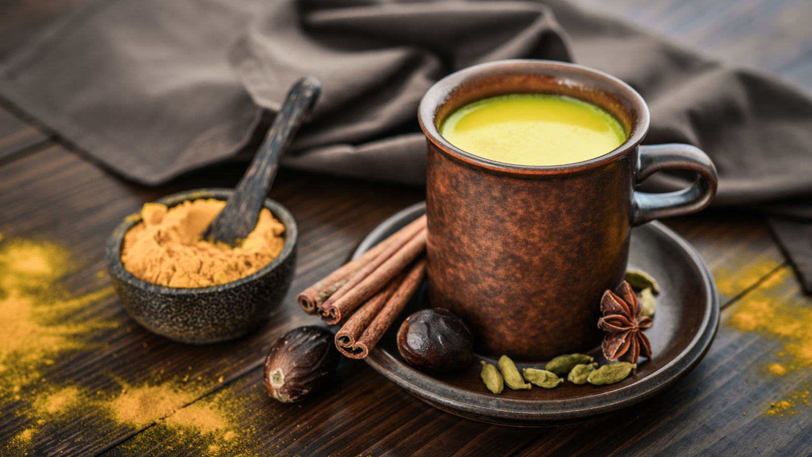 Traditional Indian drink turmeric milk is golden milk with cinnamon, cloves, pepper and turmeric on a wooden background with spices