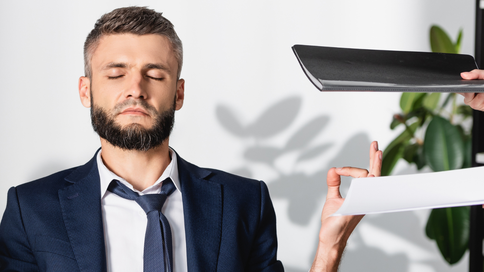 Businessman meditating near colleagues with smartphone and paper folders in office.