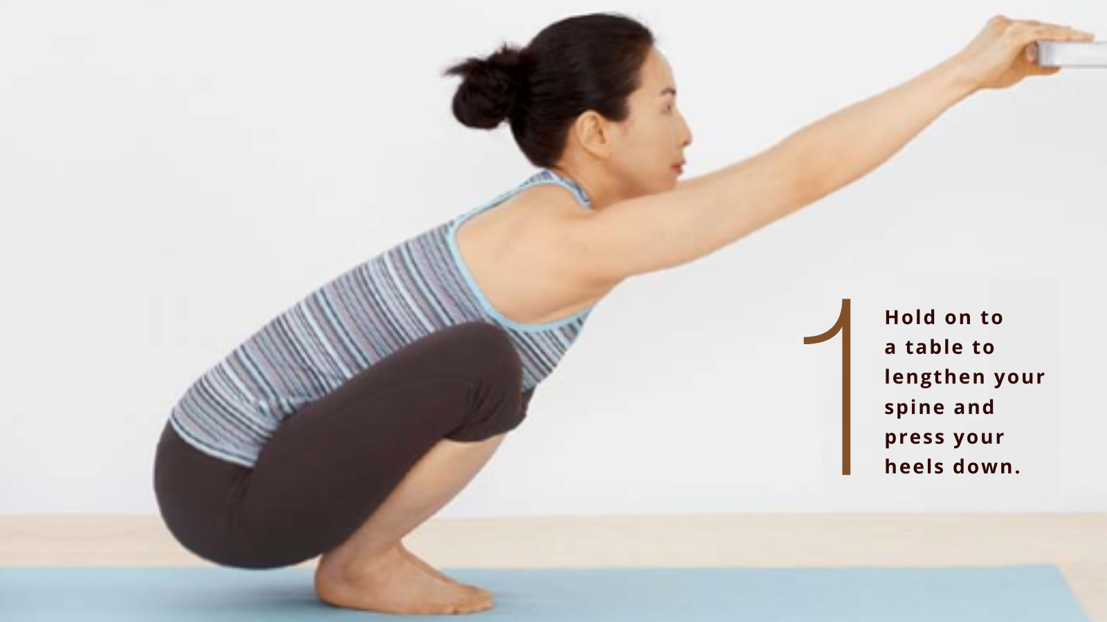 Beginning yoga student practicing a modified version of Yogic Squatting Pose (Malasana) holding on to a ledge for balance