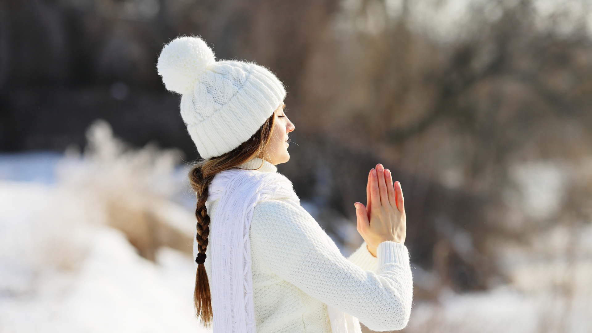 Young woman in a white hat and sweater, meditating outdoors to allow the sun and fresh air help beat off the winter blues.