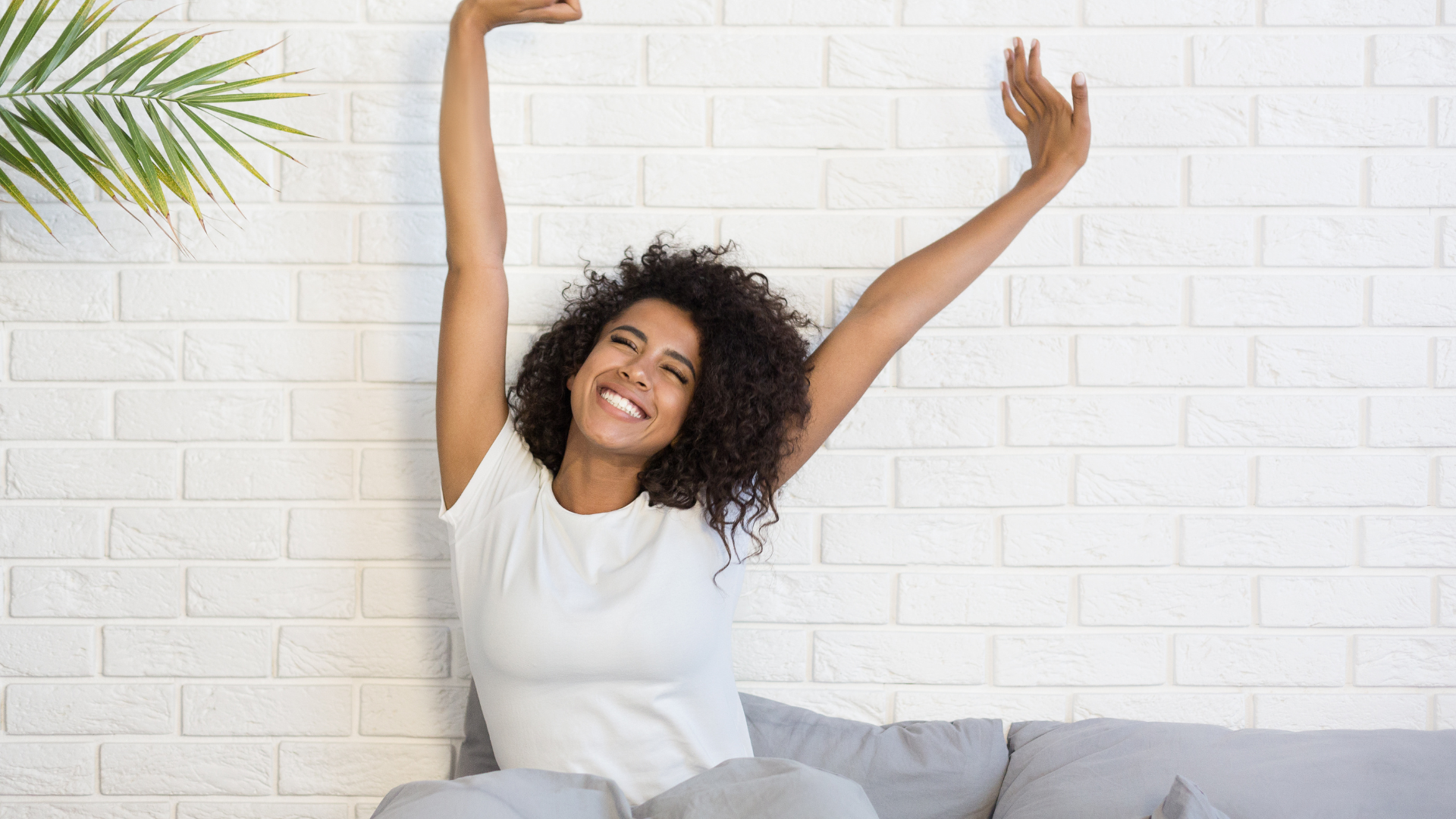 Beautiful African-American woman waking up in her bed, smiling and stretching also called Pandiculation.