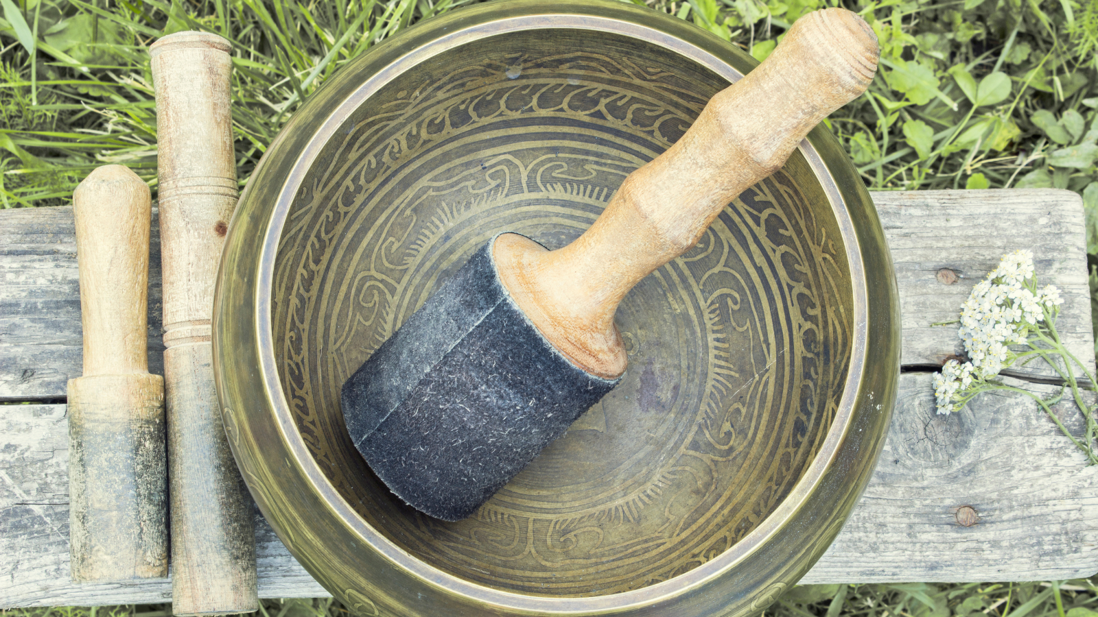 A Tibetan singing bowl with wooden mallets on a wood background.