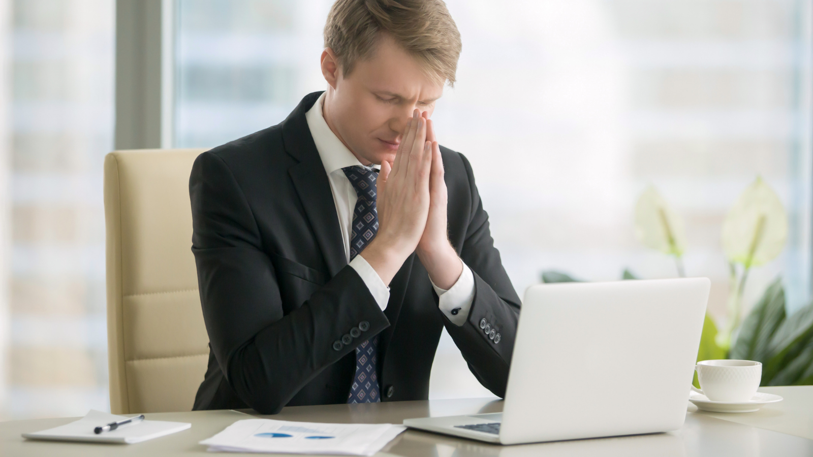 Young businessman working with laptop at desk, meditating, improving work - life balance, reduce office pressure, stress free