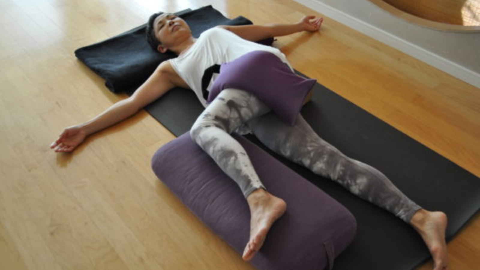  Young woman practicing Supported Supine Twist (Jathara Parivartanasana) with a blanket over her top leg.