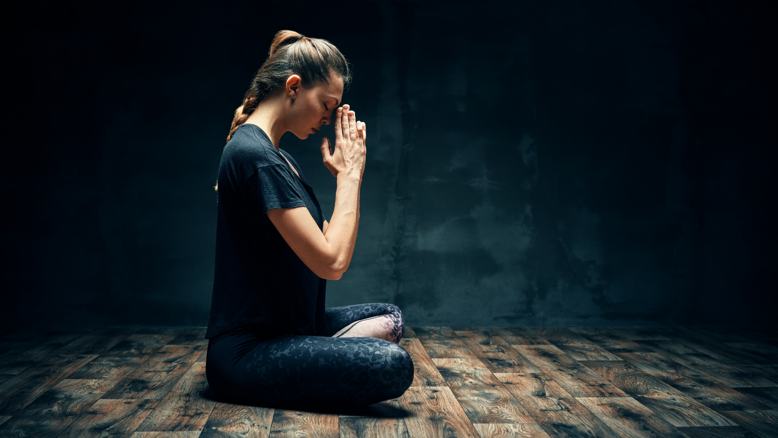 Rear view of young woman practicing yoga sitting in Lotus Pose or Ardha Padmasana Pose.