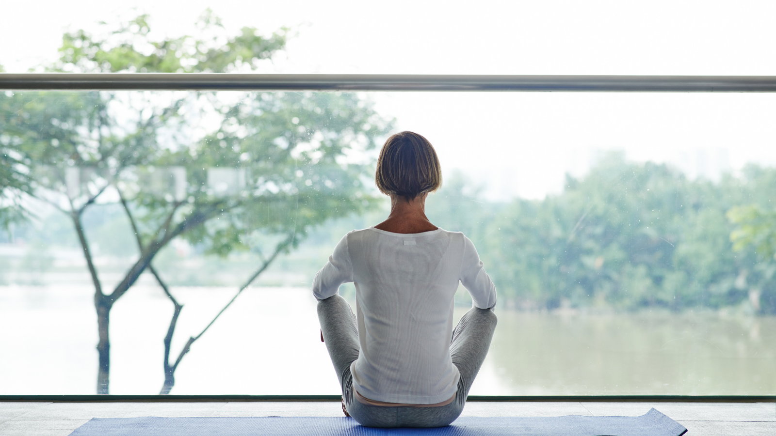 Woman meditating in front of big window, rear view.