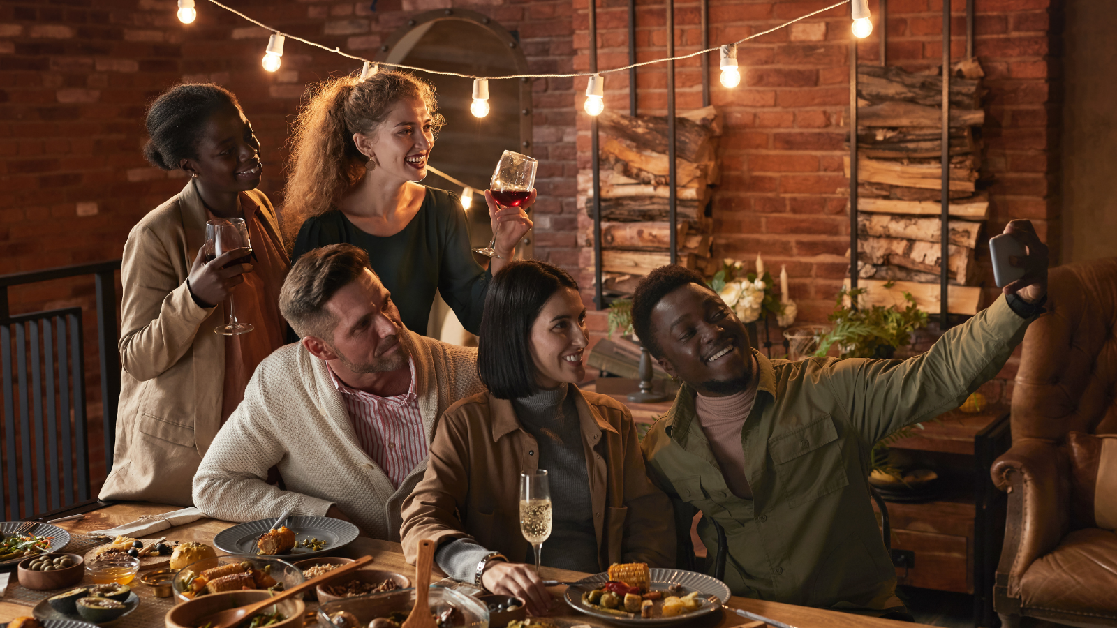 Multi-ethnic group of cheerful adult people taking selfie photo while enjoying party with beautiful lights