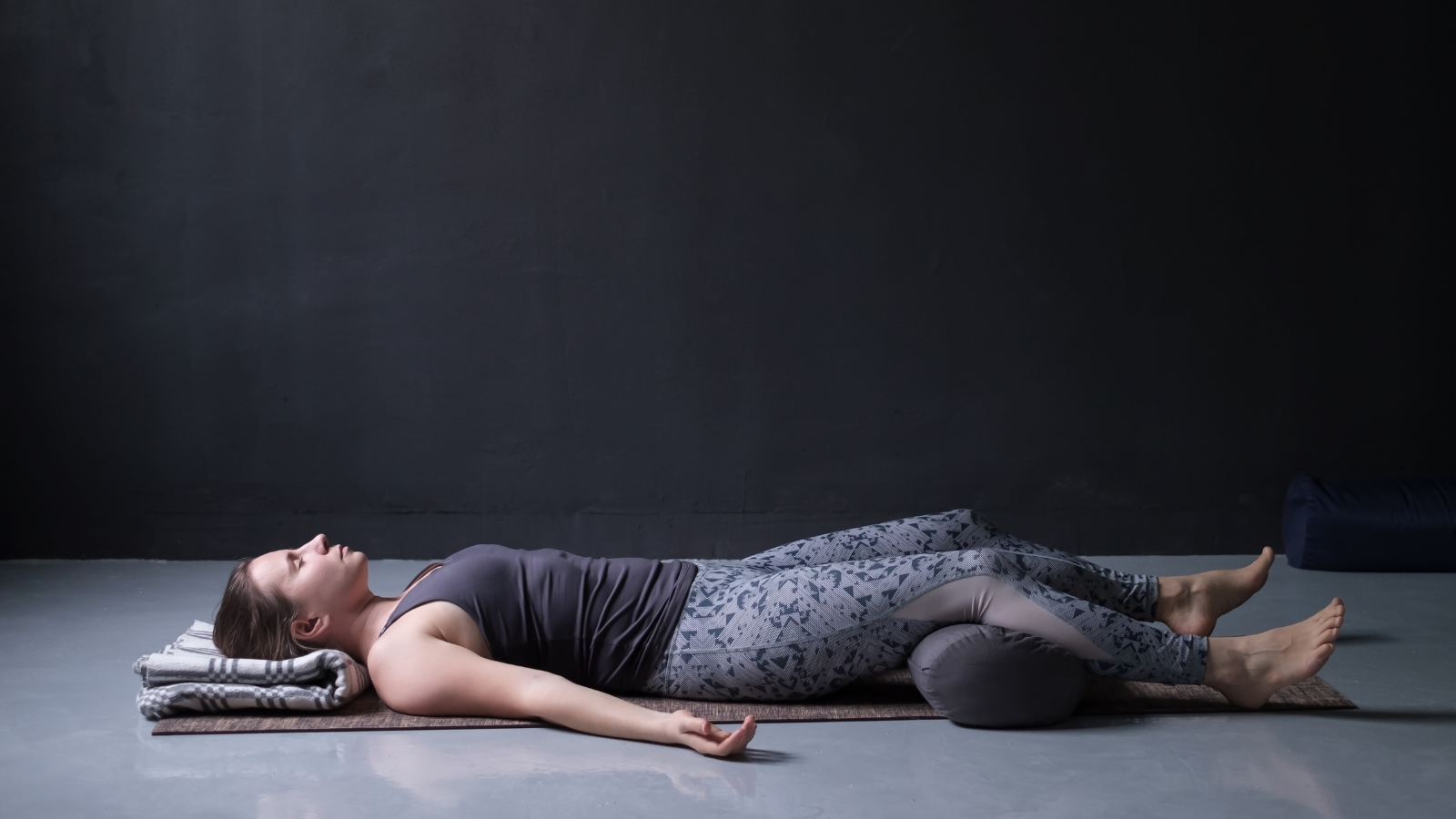 young woman working out, doing yoga exercise on wooden floor, lying in Savasana or Corpse Pose, resting after practice.