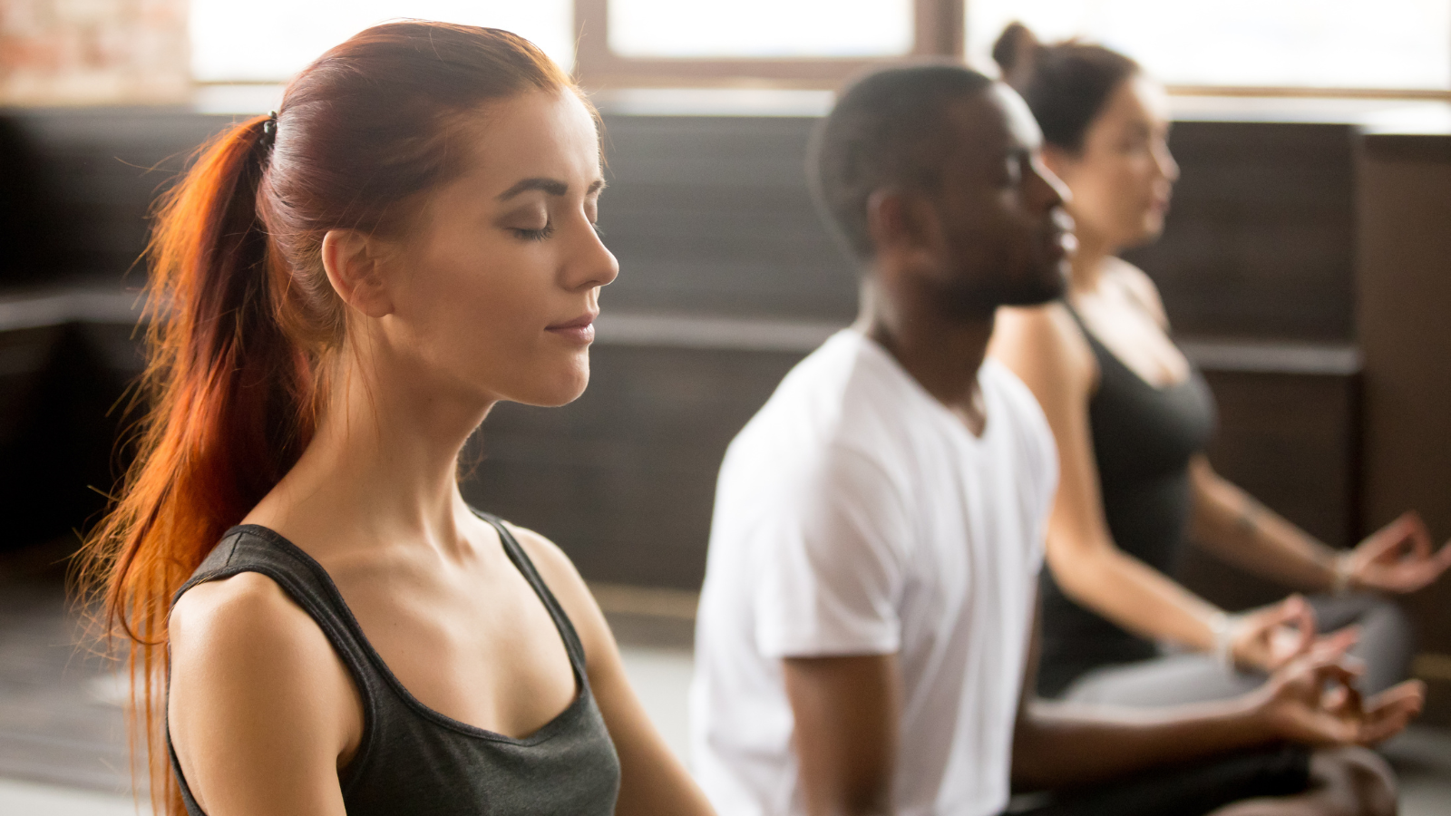 Group of young women sitting in Sukhasana exercise or Easy Sitting Pose, in yoga practice.
