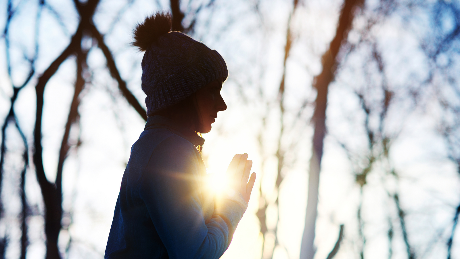 Silhouette of a meditating woman in the forest with a sun light in her hands