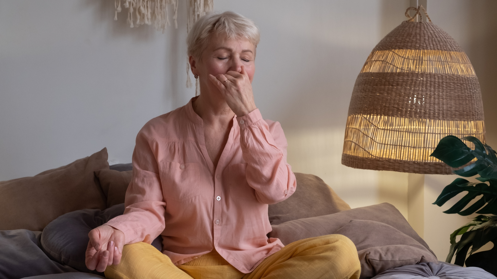 Senior woman practicing yoga at home, making Alternate Nostril Breathing or, nadi shodhana pranayama