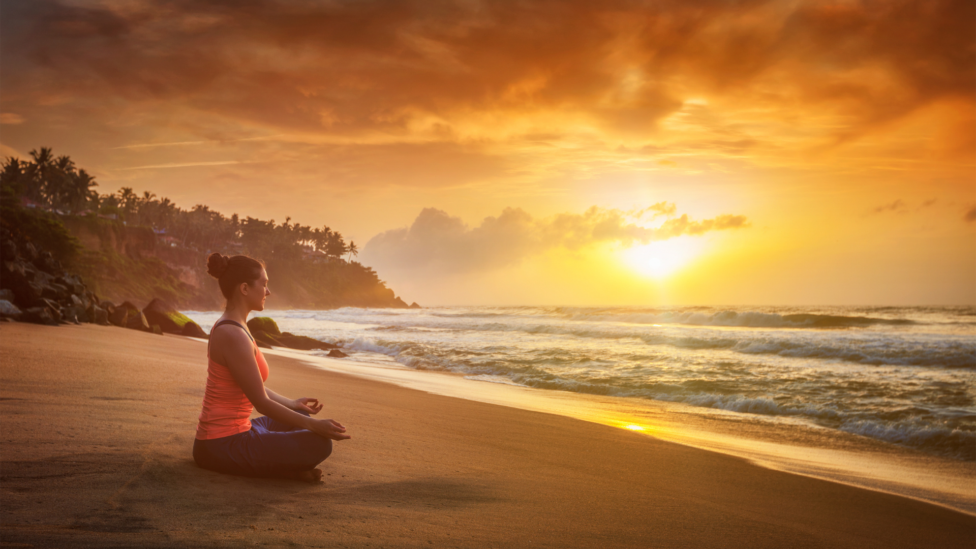 Young sporty fit woman doing yoga - meditating and relaxing in Padmasana (Lotus Pose) with Chin Mudra outdoors at tropical beach on sunset 