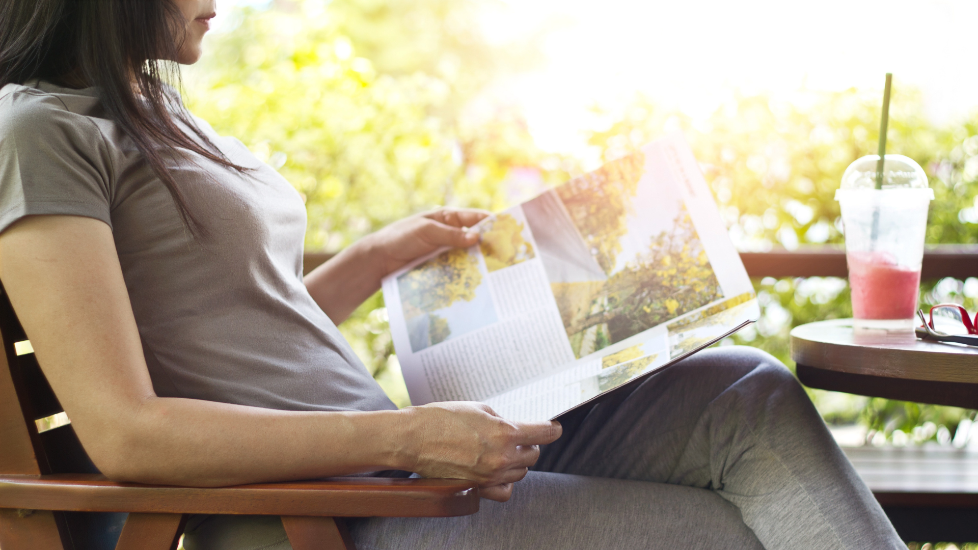 woman relaxing by reading travel magazines with strawberry smoothie on table, nature background. Contentment for those quiet moments.