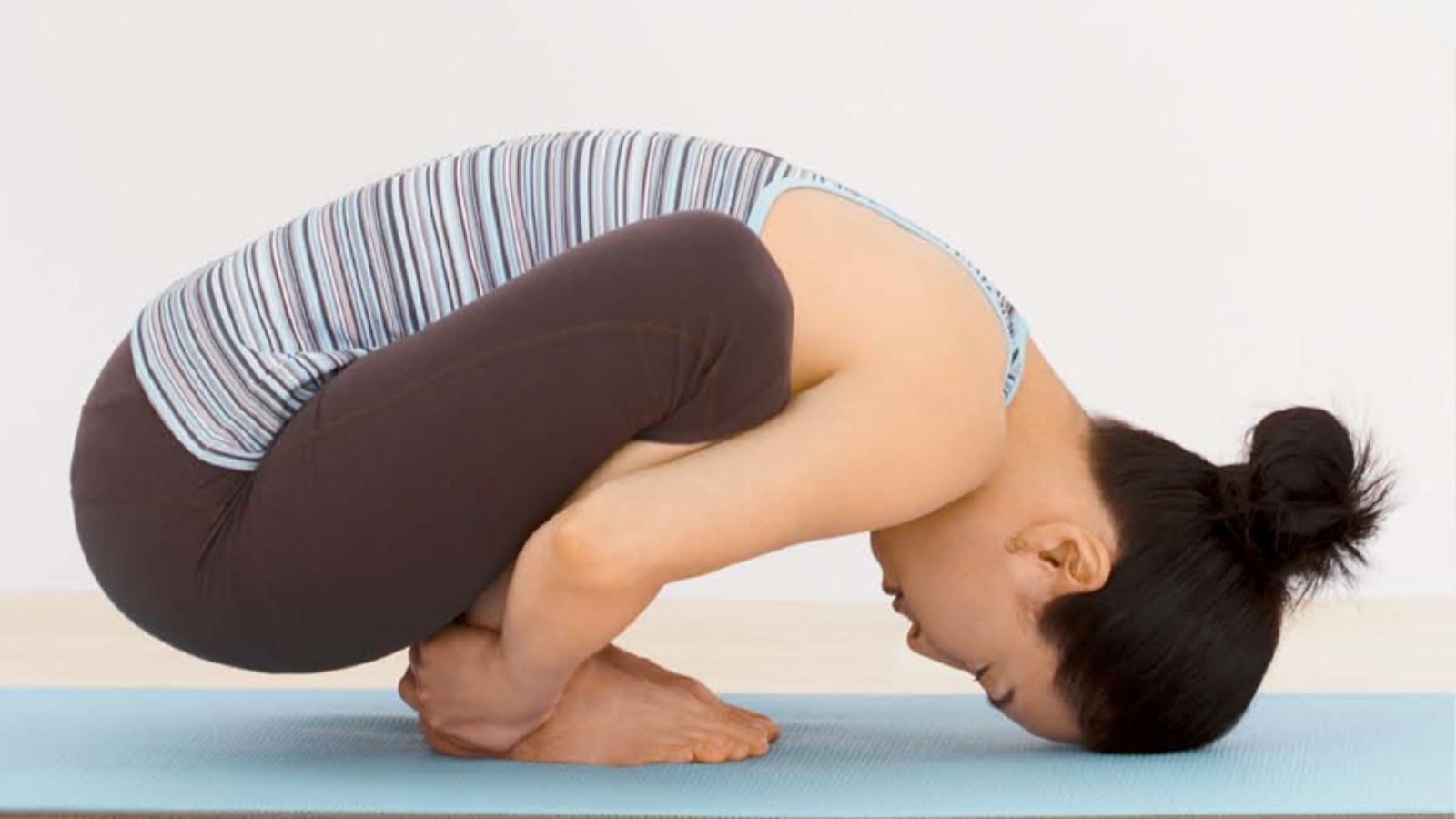 Yoga student practicing the final version of Yogic Squatting Pose (Sanskrit name: Malasana) with head touching the mat