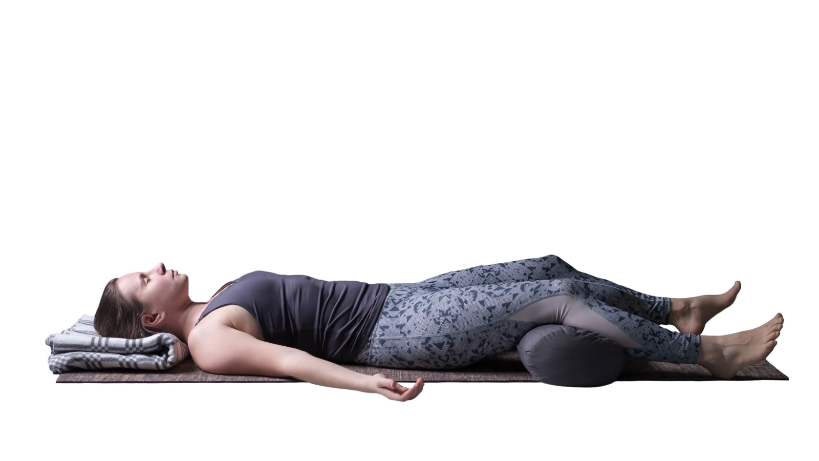 Young woman working out, doing yoga exercise on wooden floor, lying in Savasana or Corpse Posture