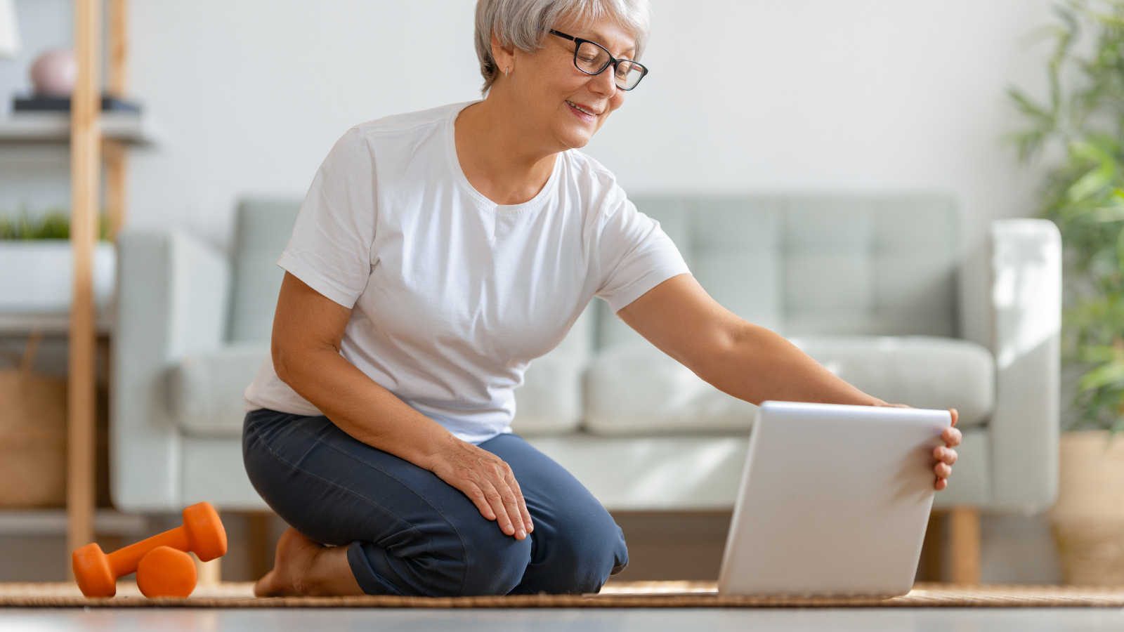 Senior woman in activewear watching online courses on laptop while exercising at home