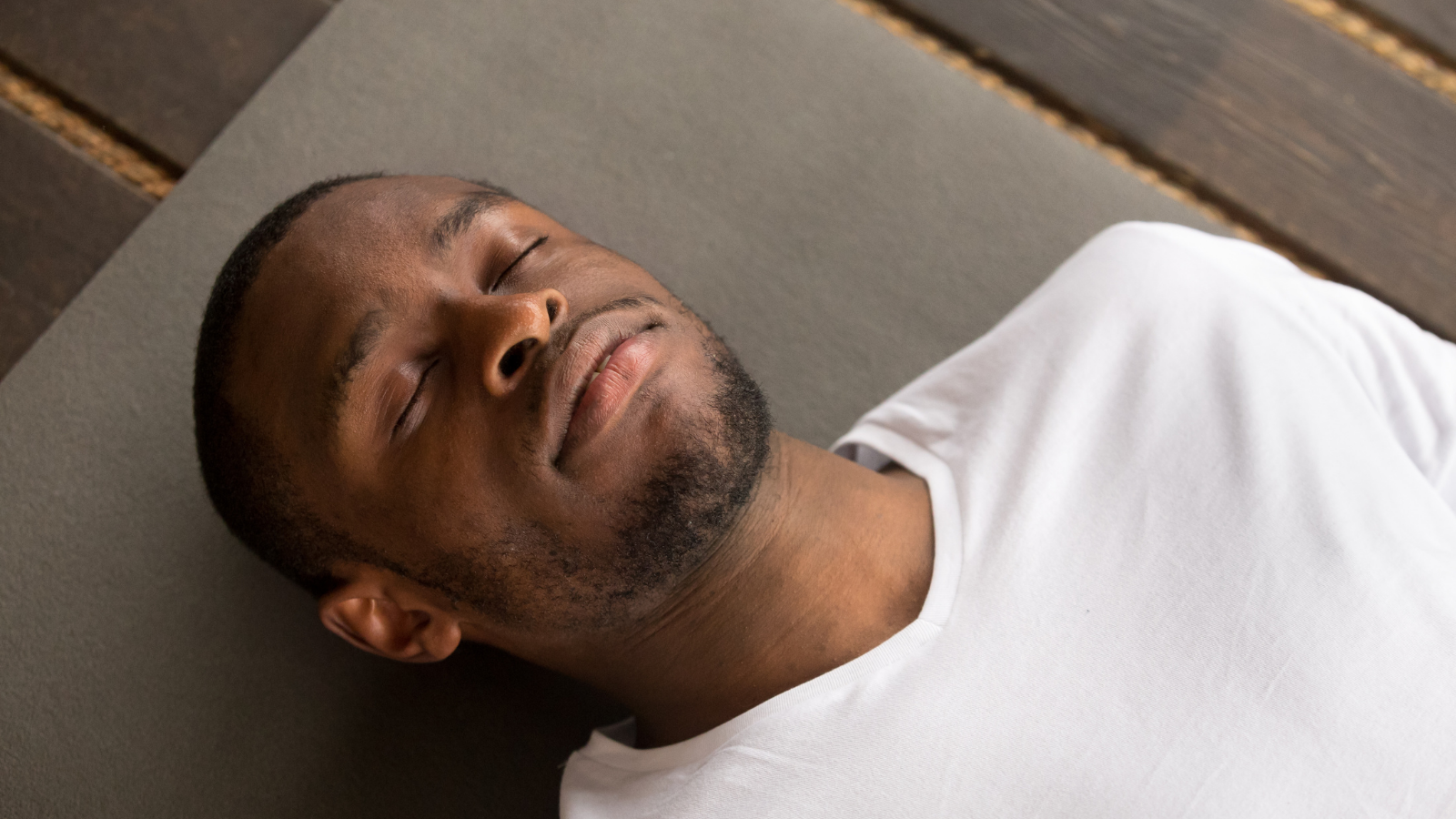 Photo of young black man lying in or Corpse Pose or Savasana, with his eyes closed