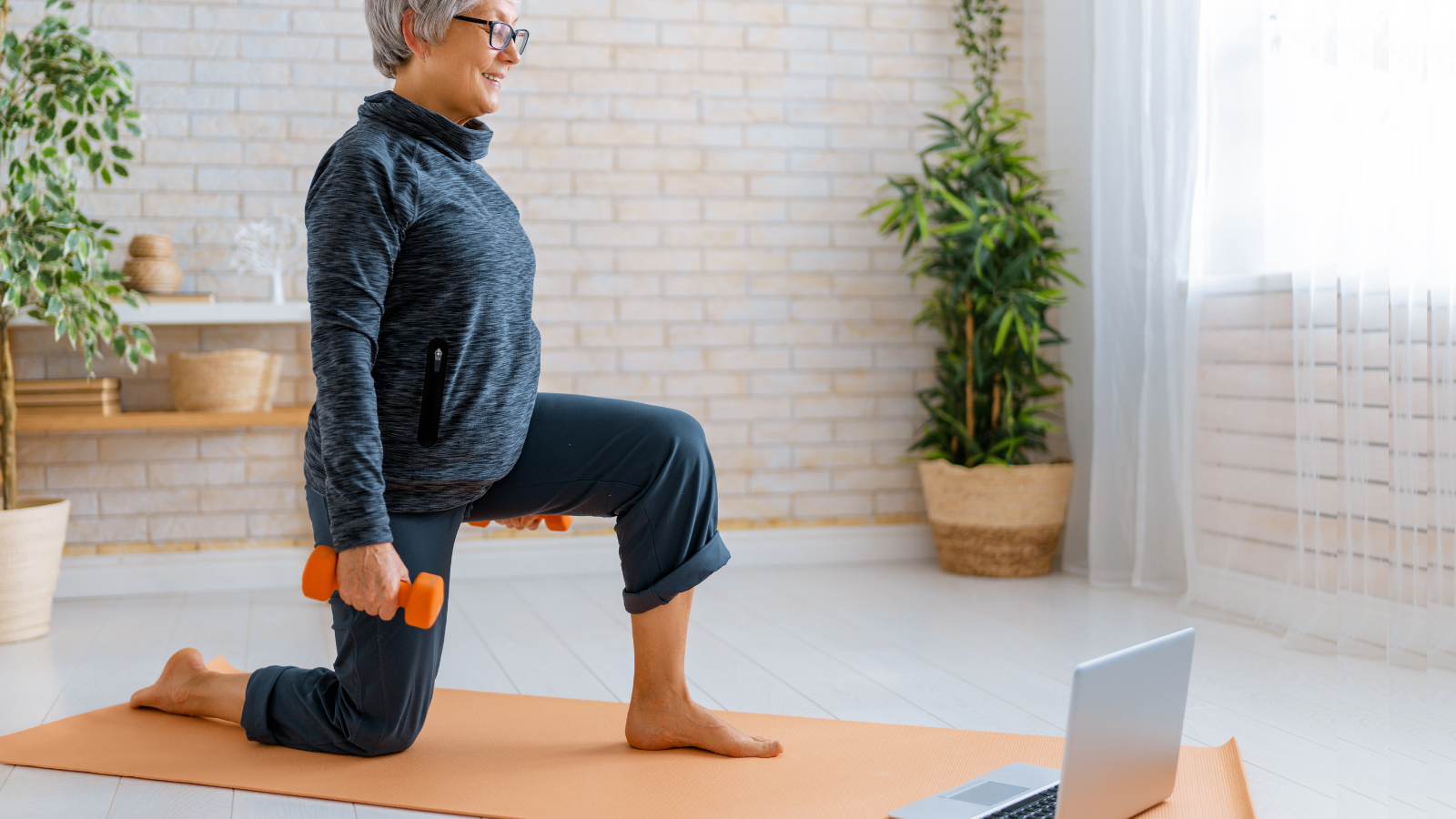 Senior woman in activewear watching online courses on laptop while exercising at home