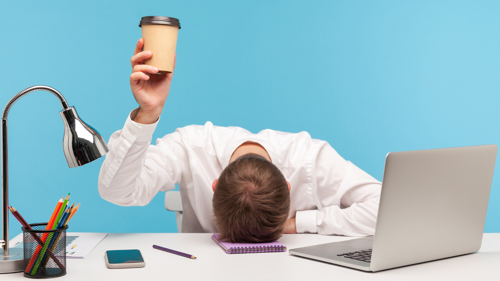 Exhausted male employee feeling fatigue lying on table and raising coffee cup, lack of energy in morning office