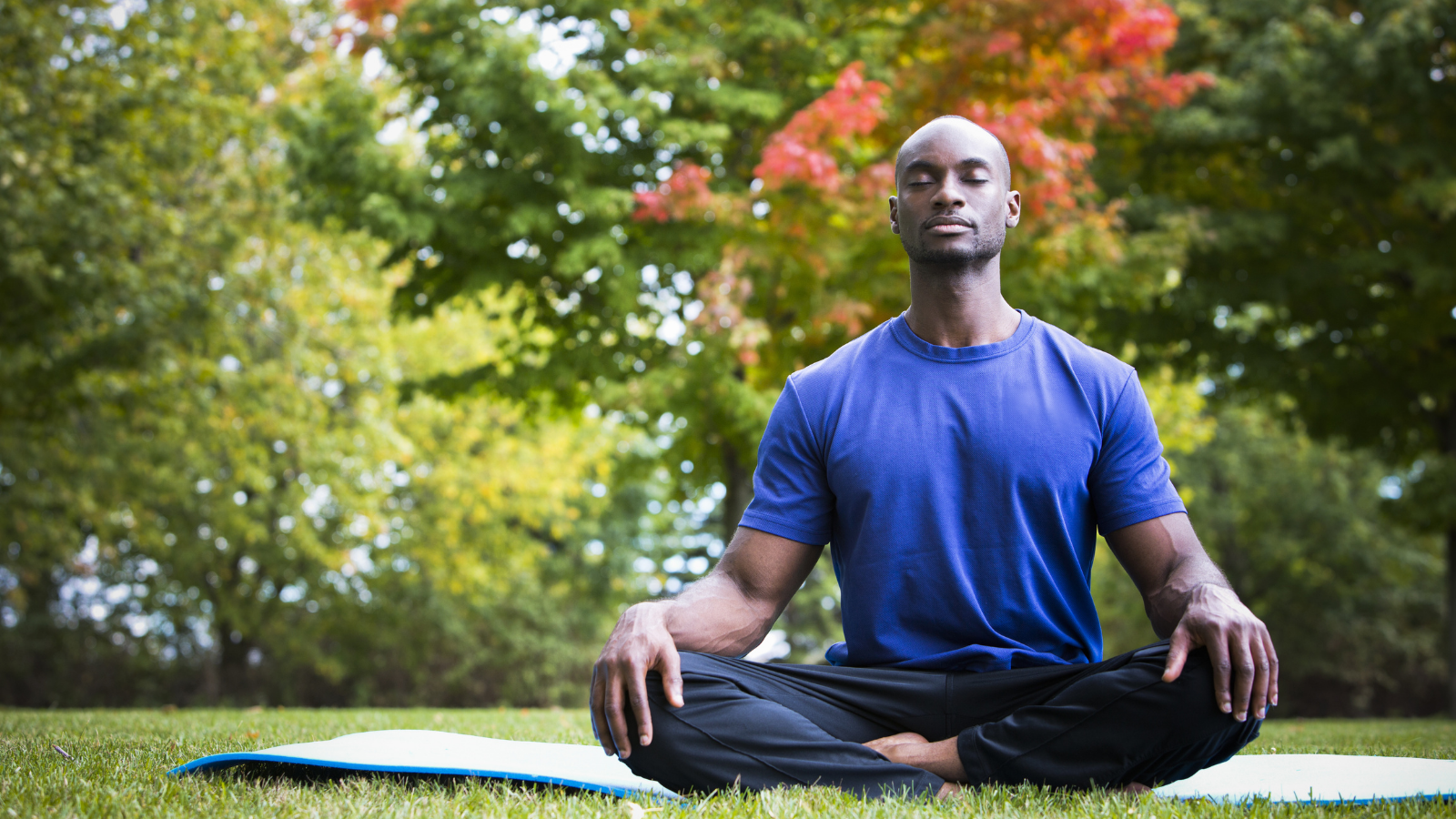 young black man wearing athletic wear sitting in the park doing yoga meditation.