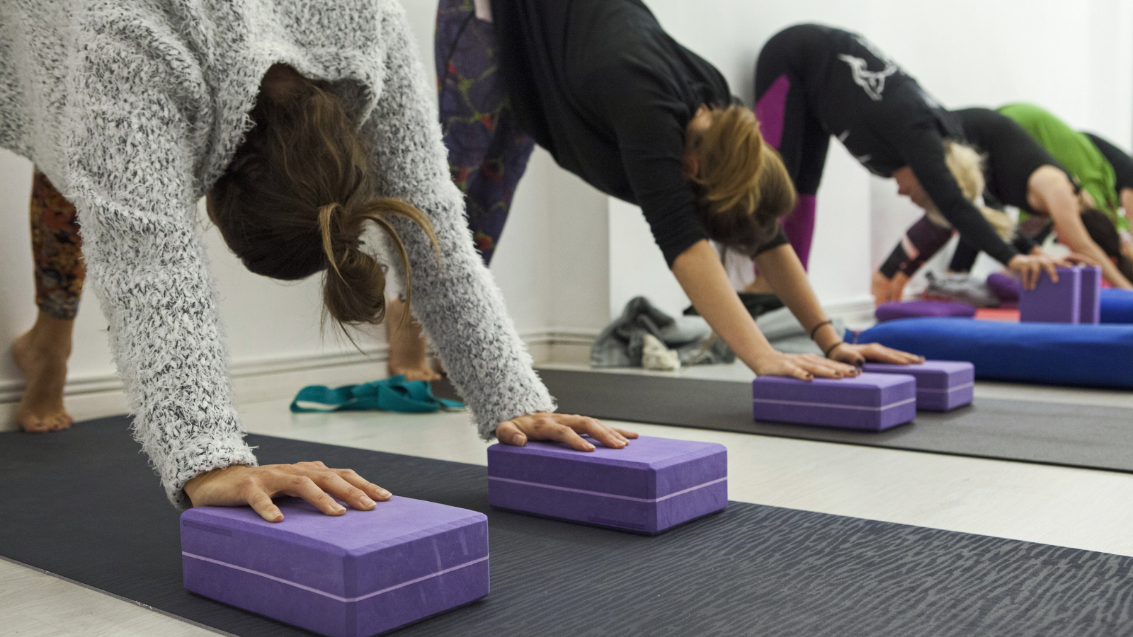 Women practicing yoga therapy, stretching in Down Dog Pose using blocks and the wall.