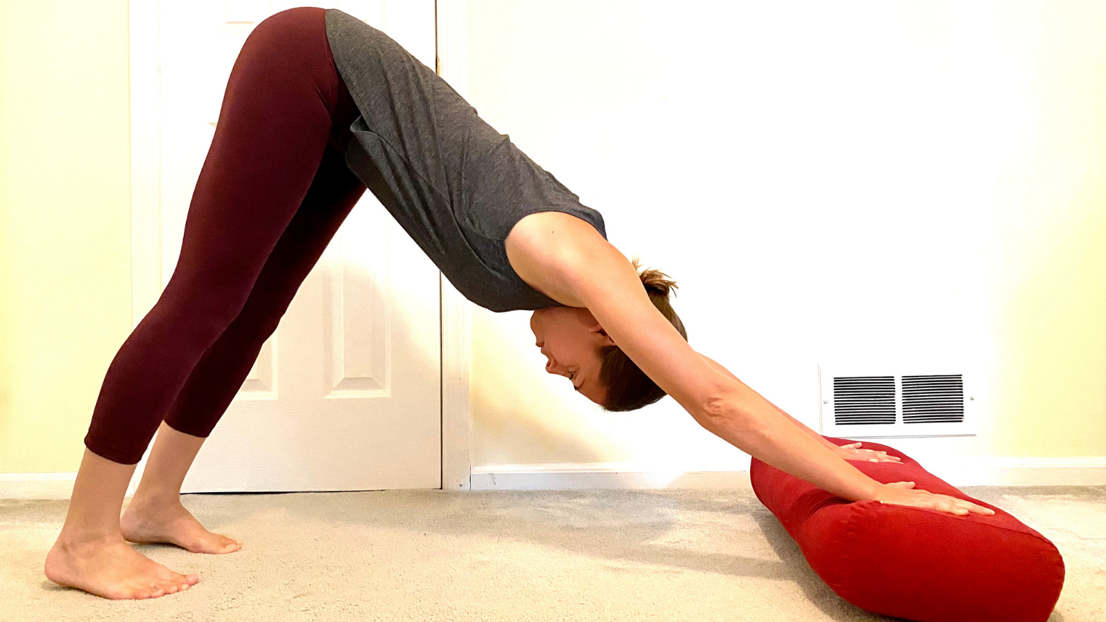 Variation of Downward Facing Dog (Adho Mukha Svanasana) adding a bolster under the hands to create more comfort and space