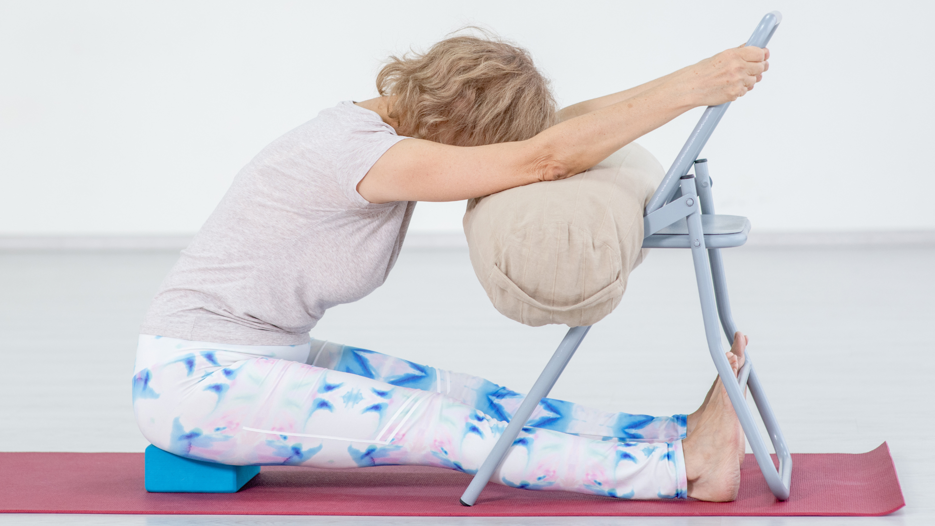 Woman practicing a supported forward bend known for calming stress and anxiety, one of the benefits of restorative yoga poses.