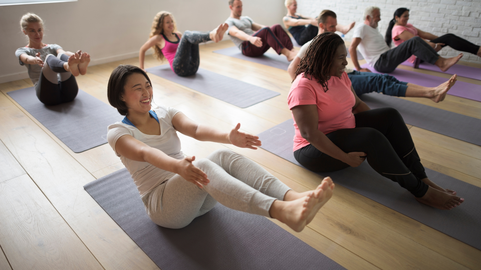 Diverse class of yoga students practicing accessible variations of Boat Pose or Navasana.