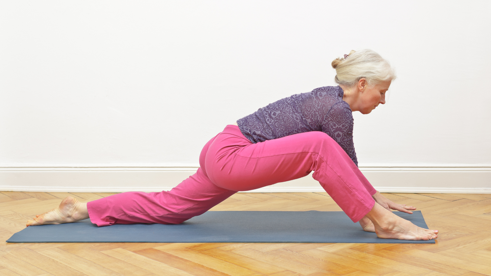 Senior woman with gray hair doing yoga exercise at home in front of a white wall