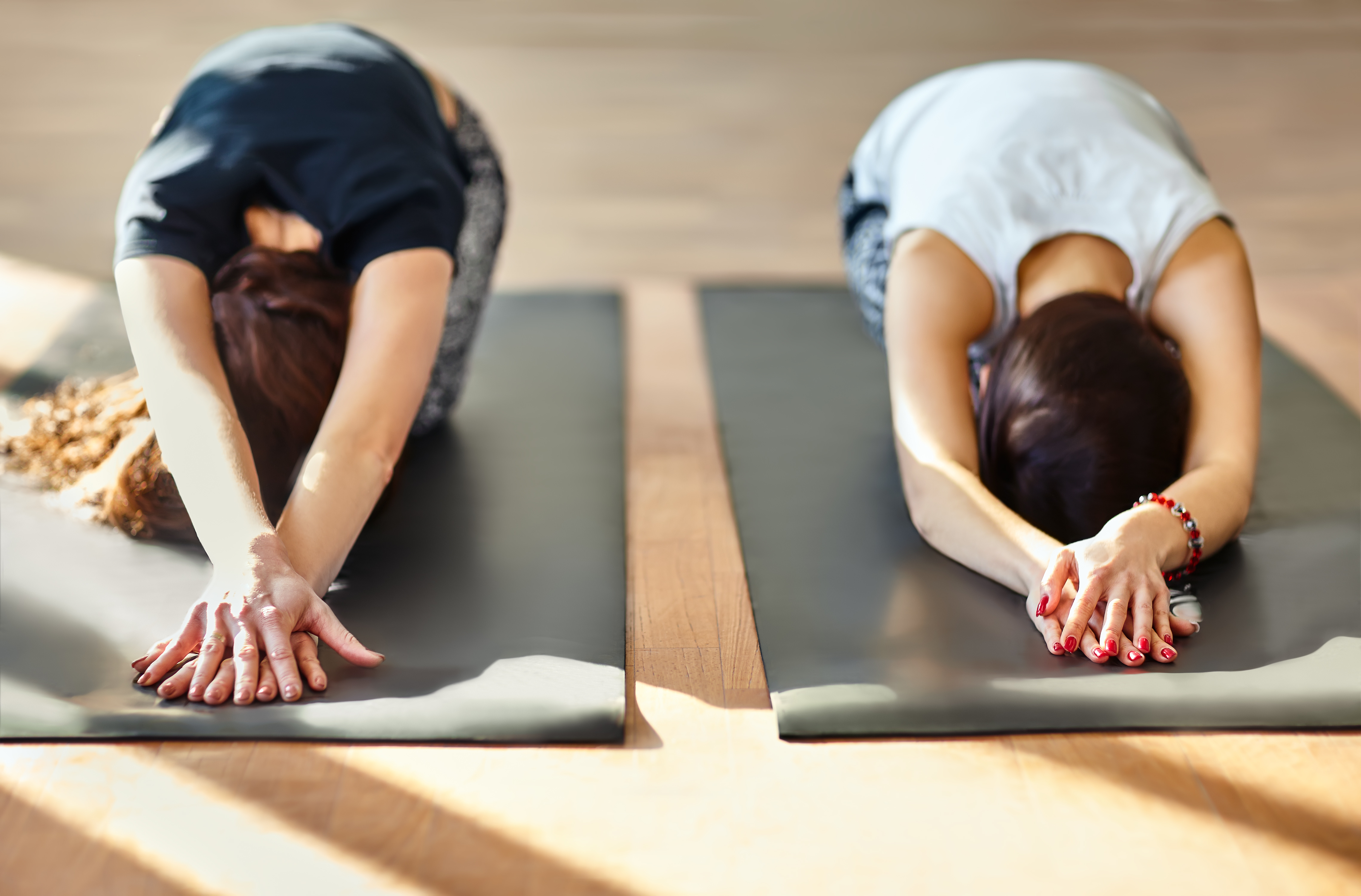 Two women practicing relaxing yoga, in Child's Pose (Balasana)