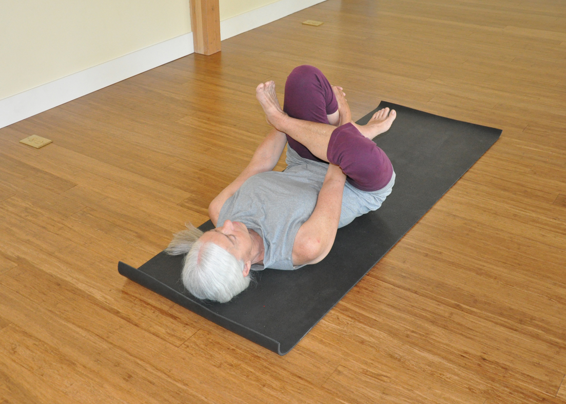 Woman practicing pigeon pose (eka pada rajakapotasana) alternative in Supine Half Lotus (Supta Ardha Padmasana) yoga pose to open the hip and chest and bend the back