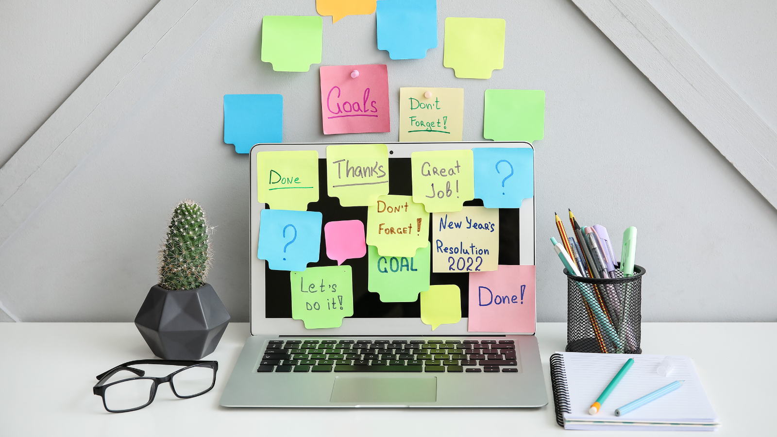 Modern workplace with laptop and sticky notes near light wall