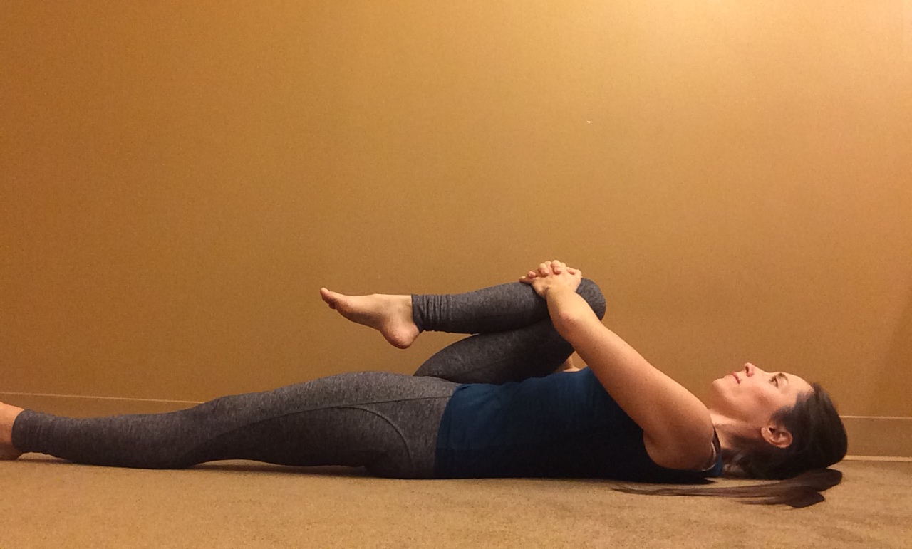 A woman in Knee-to-Chest Pose (Apanasana), a yoga pose to massage the psoas muscle