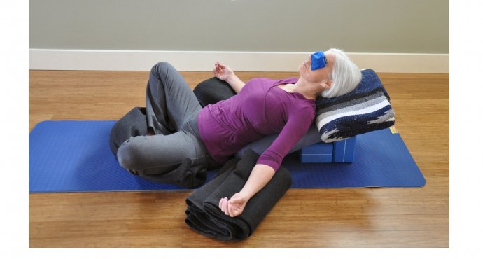 A woman in a supported variation of Reclined Bound Angle Pose (Supta Baddha Konasana) with blankets and blocks under arms, head, and legs