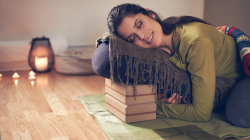 Serene lady practicing a restorative pose and meditating on a yoga mat with props