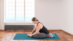 Image depicts a forward fold in Cobbler's Pose or Baddha Konasana.