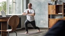 Senior hispanic man standing in warrior yoga pose variation practicing in living room alone