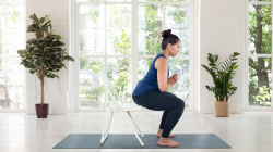Woman practicing Chair Pose Utkatasana on a folding chair.