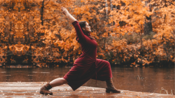 curvy woman practicing warrior 1 on dock near lake and autumn fall leaves