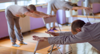 Mature yoga students practicing half forward bend with the support of chairs. 