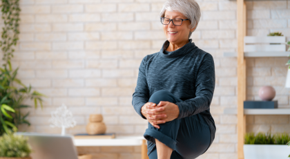 Senior woman in activewear watching online courses on laptop while practicing strengthening poses at