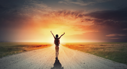 woman raising her arms in joy walking on road towards a sunset, depicting feeling of self-healing