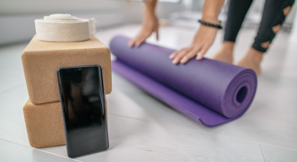 Student rolling out mat getting ready for yoga class with mobile smartphone close by