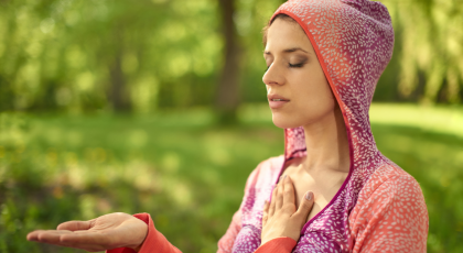 Portrait of beautiful woman meditating and doing yoga at sunset on the grass in a park or forest