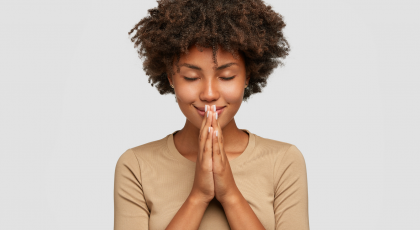 Beautiful young black woman stands in meditative pose, holds hands in Anjali Mudra