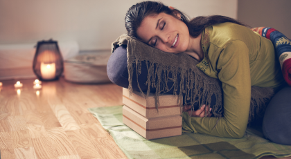 Serene lady practicing a restorative pose and meditating on a yoga mat with props