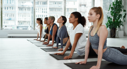 Image depicts a diverse group of yoga students at class practicing Bhujangasana or Cobra Pose.